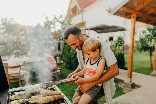 A father and son tending the grill on their back porch