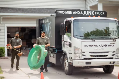 junk haulers walking past a junk removal company junk truck finishing a decluttering cleanout service on a customers home