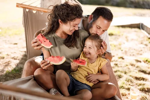 A family enjoying watermelon on the hammock in their cleared out and perfectly landscaped back yard