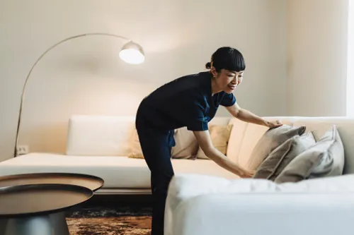 A woman is tidying up her living room by organizing the couch pillows