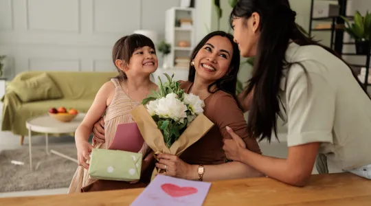 Two daughters give their mom a card and flowers for Mother's Day