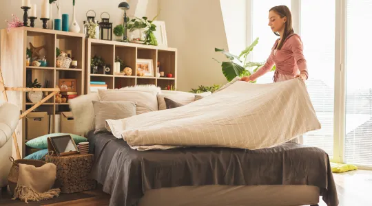 Woman lays comforter down while making bed 