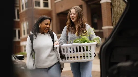 Two college students carry a basket of items to move out